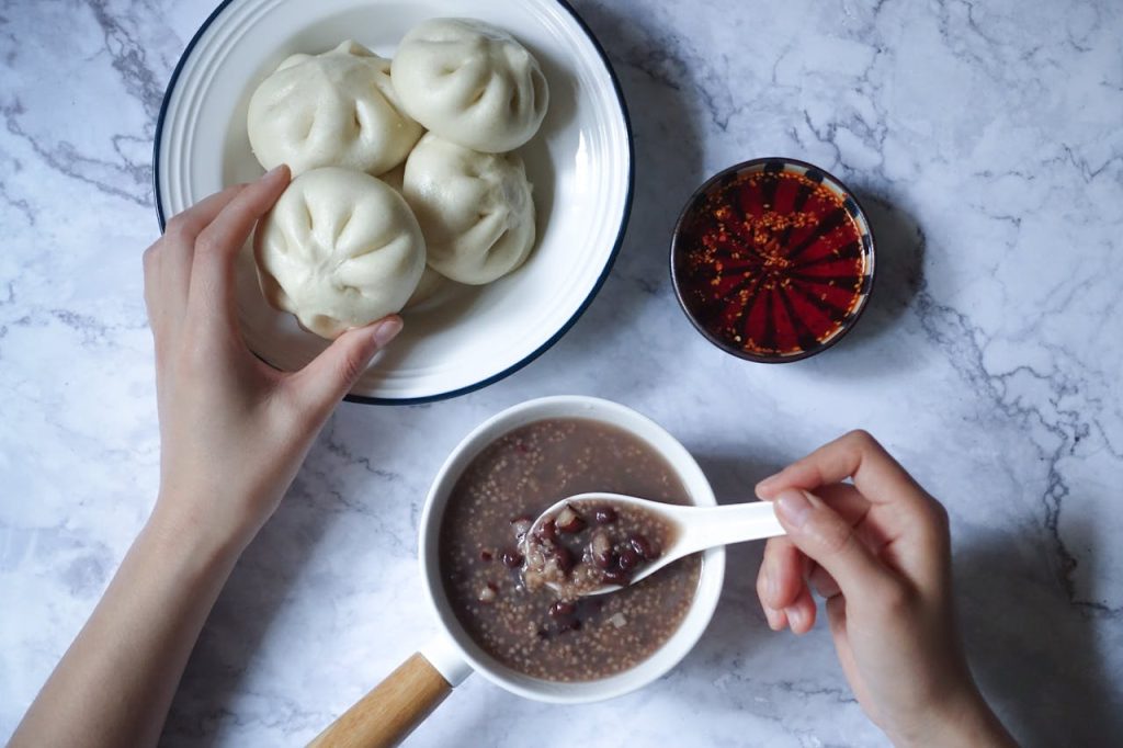 A top-view of a traditional Asian breakfast featuring steamed buns and red bean porridge.